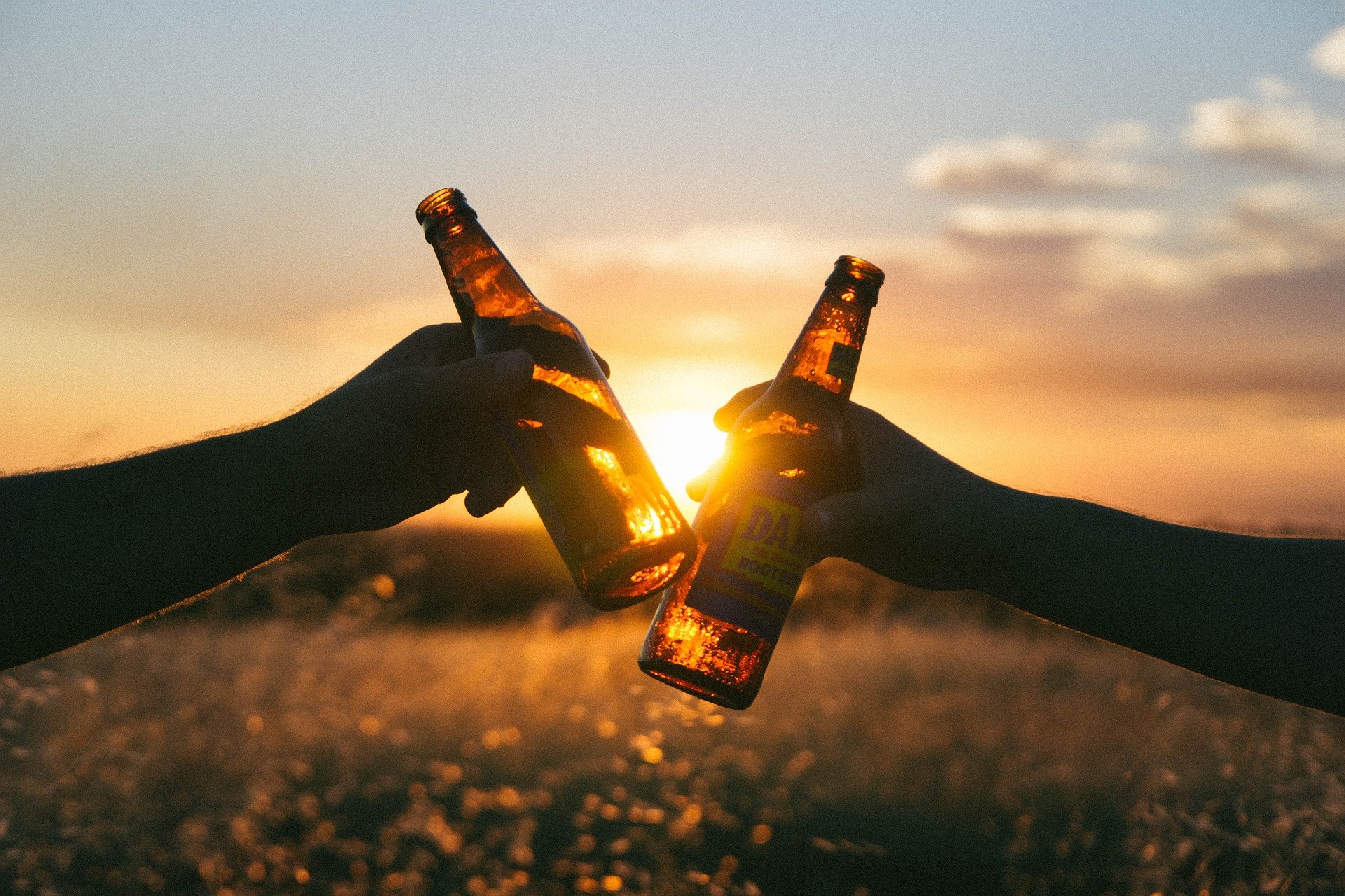 Zwei Hände stoßen bei Sonnenuntergang mit Bierflaschen an.