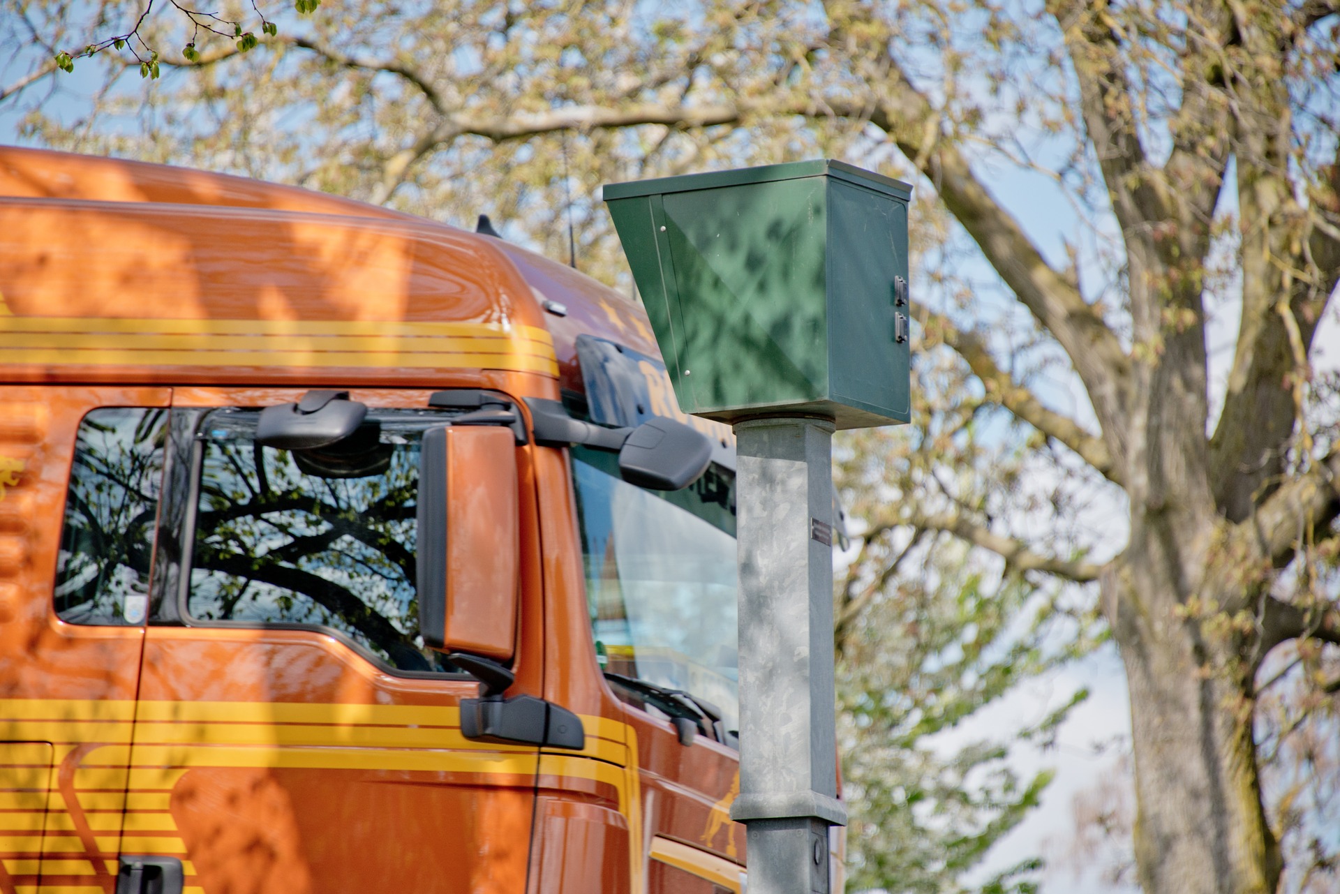 Orangefarbener Lastwagen fährt an einem grünen Geschwindigkeitsmessgerät vorbei.